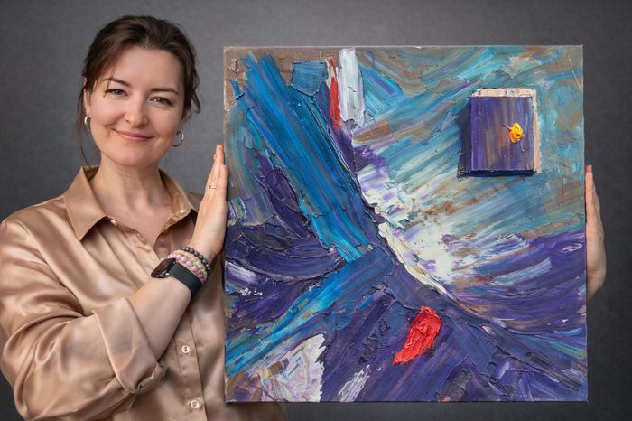 Artist Vlady Zinkovska holding abstract painting in Calgary studio